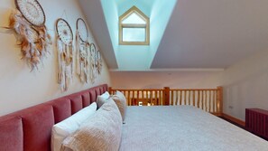A bedroom with a sloped ceiling, a skylight, a bed with pillows, and a wall with dreamcatchers.