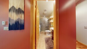 Ein Flur, der zu einem Badezimmer mit Dusche, Toilette und Regalen führt.