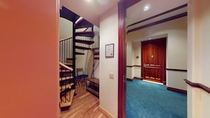 A staircase with a wooden handrail and a blue carpeted floor leading to a door with a wooden frame.