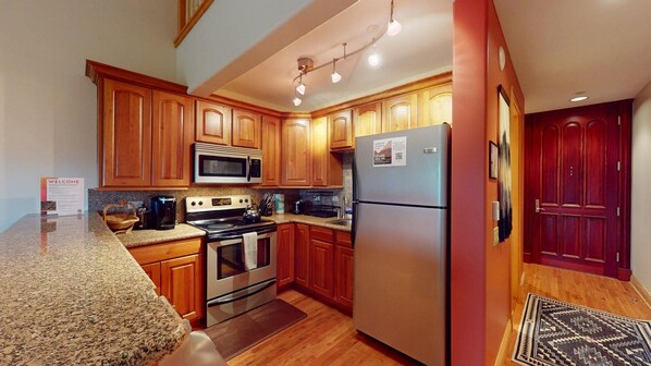 A kitchen with wooden cabinets, stainless steel appliances, granite countertops, and a red door.