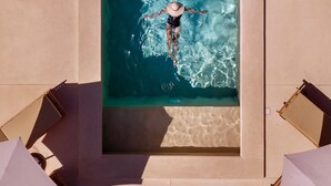 Eine Vogelperspektive zeigt einen rechteckigen Swimmingpool mit klarem, blauem Wasser, umgeben von Liegestühlen und einer gefliesten Terrasse.