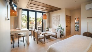 Ein modernes Hotelzimmer mit Bett, Sofa, Essbereich und großem Fenster mit Blick auf Palmen.