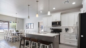 A modern kitchen with white cabinets, a central island with stools, stainless steel appliances, and pendant lighting.