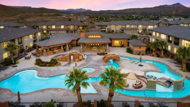 A resort with multiple buildings, a large swimming pool, and a mountainous backdrop.