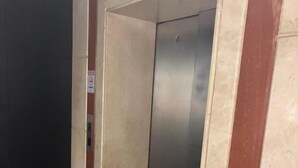 Un ascensor con una pantalla digital, un basurero y una pared con un cartel de prohibido fumar.