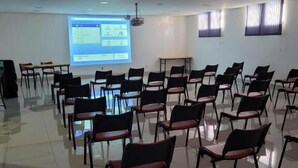 Un salón de conferencias con filas de sillas, una pantalla de proyector mostrando una presentación y una pizarra.