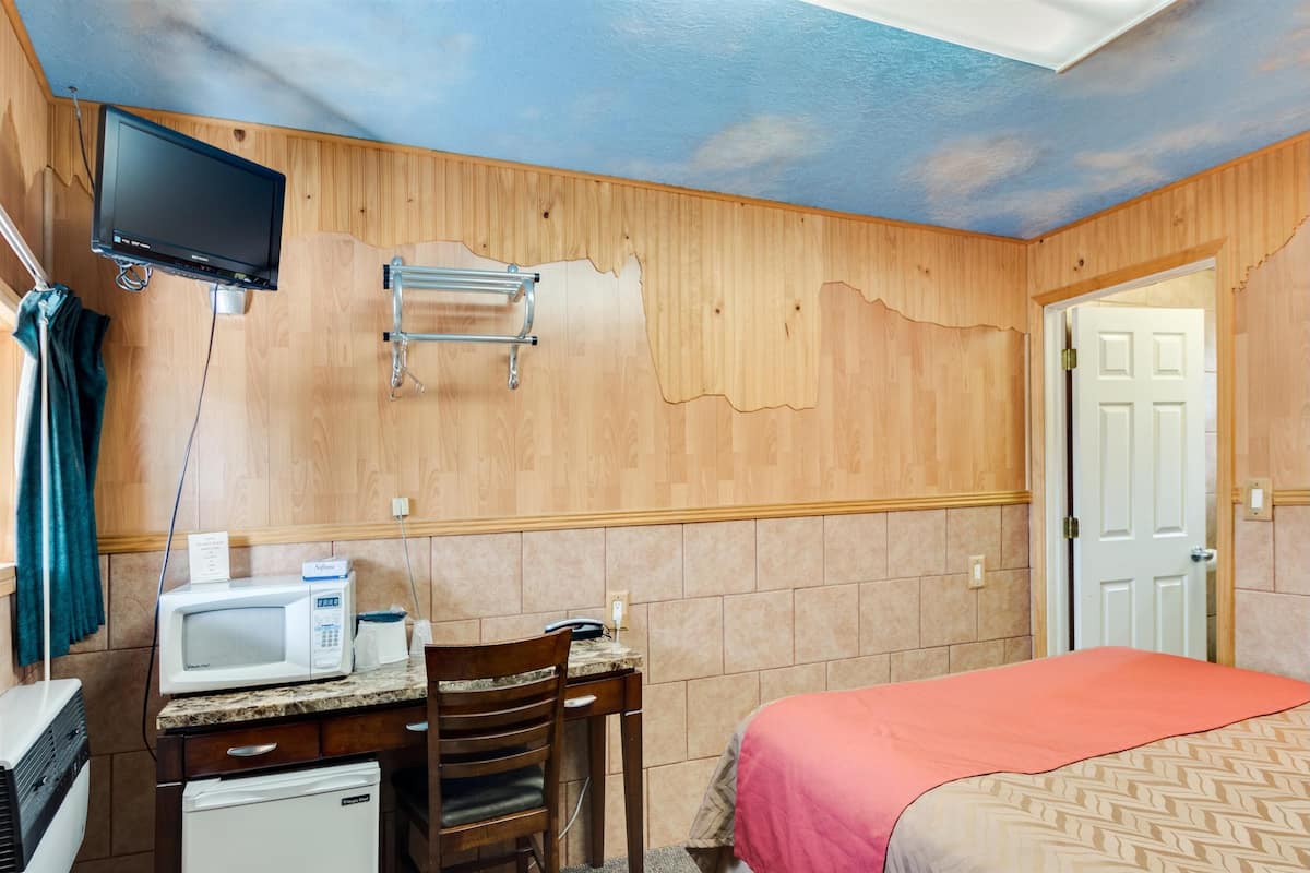 A compact hotel room with a kitchenette, a bed, a TV mounted on the wall, and a door leading to another room.
