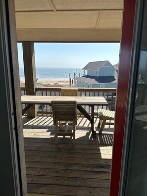 Um deck de madeira com mesa e cadeiras, com vista para uma praia e uma casa.