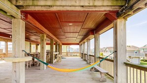 A wooden deck with a hammock, wooden pillars, and a view of houses in the background. - 1 Block from the Beach, Entertainment Deck with games and Tv, large enough for 26 guests. (Bolivar Peninsula)