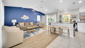 Una sala de estar moderna con una pared azul de acento, un sofá, una mesa de centro y una zona de cocina con barra y taburetes.