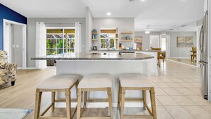 Una cocina moderna con una isla central, taburetes de bar y un comedor con vistas al exterior.