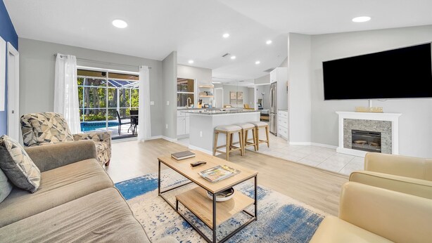 Una sala de estar moderna con sofá, mesa de centro y televisor. Hay una cocina con comedor y chimenea.