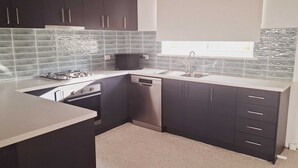 Una cocina compacta con armarios oscuros, lavavajillas, microondas y fregadero.