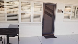 Un edificio blanco con puerta y ventanas. Hay una mesa y una silla afuera.