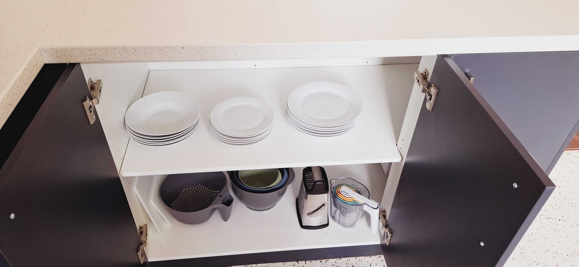 A kitchen cabinet with white plates, bowls, and a grater.