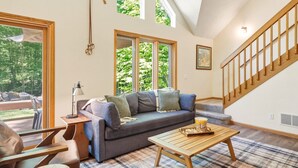 A spacious living room with a large gray sofa, a wooden coffee table, and a staircase. - Up North Chalet | Ac | Bbq | Bikes (Cedar)