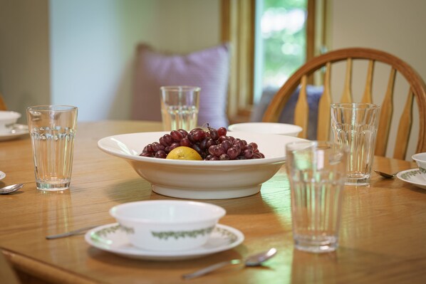 Una mesa de comedor con un bol de uvas y un limón, vasos y una taza sobre una mesa de madera.