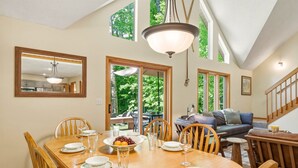 A dining area with a wooden table set for four, a large mirror, and a view of the outdoors through a glass door. - Up North Chalet | Ac | Bbq | Bikes (Cedar)