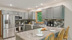 A modern kitchen with stainless steel appliances, a granite countertop, and wooden chairs. - Up North Chalet | Ac | Bbq | Bikes (Cedar)