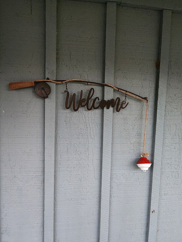 A rustic welcome sign with a wooden handle and a small bell, mounted on a weathered wooden wall. - Riverfront! Snappin Turtle Cabin, Balcony-Floating dock-Fishing. (Steinhatchee)
