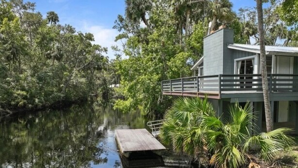 Una casa vicino a un fiume tranquillo, con un pontile, immersa nel verde.