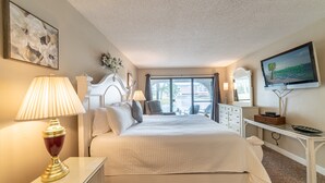 A hotel room with a large bed, a TV, a desk with a lamp, and a view of the outdoors.