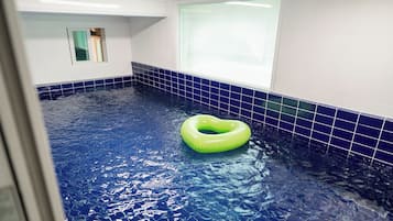 Una piscina con un flotador verde, paredes de azulejos y una ventana.