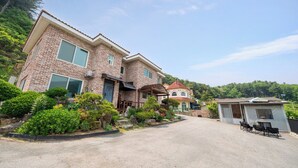 A two-story brick house with a covered porch, a small attached structure with a red roof, and a gravel driveway. - Gapyeong Dream Pool Villa Pension (Gapyeong)