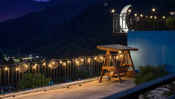 A nighttime view of a balcony with a swing chair, string lights, and a view of the mountains. - Gapyeong Dream Pool Villa Pension (Gapyeong)