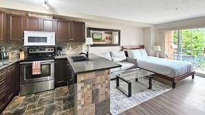 A modern kitchen with a central island, a dining area, and a bedroom with a large window.