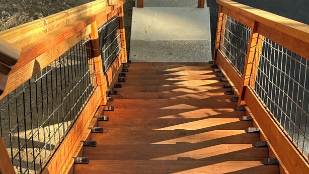 Una escalera de madera con barandales de metal que conduce a una zona cubierta.