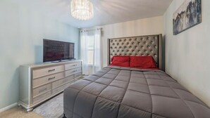 Una camera da letto con testiera trapuntata, una televisione su un comò e un lampadario.