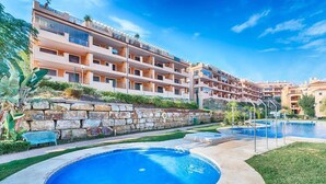 A modern hotel with a swimming pool, stone wall, and multiple balconies.