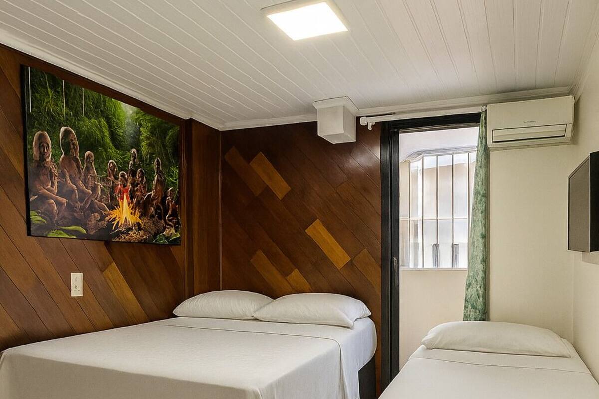 A hotel room with two beds, a large wall mural, a ceiling light, and an air conditioning unit.