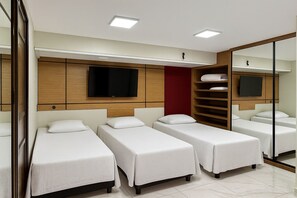 A hotel room with four single beds, a large mirror, a TV mounted on the wall, and built-in wooden shelves. - Hotel COP30 (Belém)