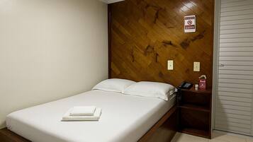 A bedroom with a bed, wooden headboard, white walls, and a tiled floor.