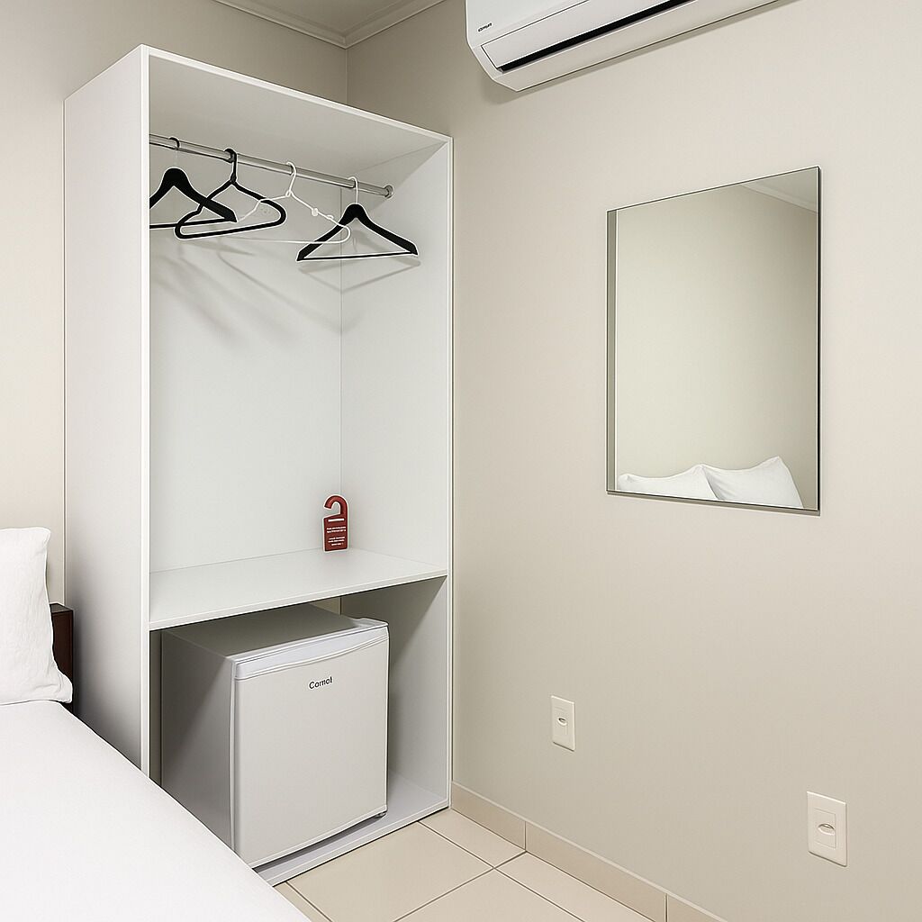 Un armario blanco con un refrigerador pequeño, un espejo y una percha para ropa.