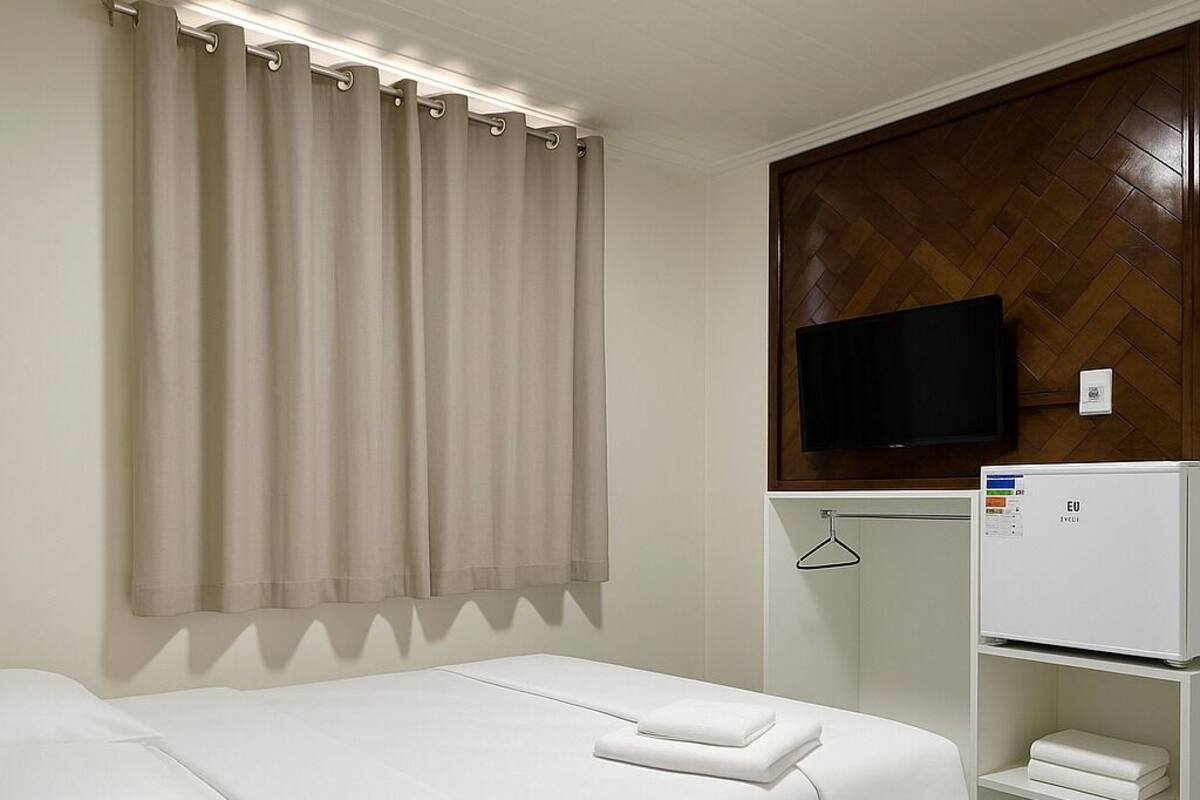 A hotel room with a bed, a TV, a minibar, and a wooden wall panel.