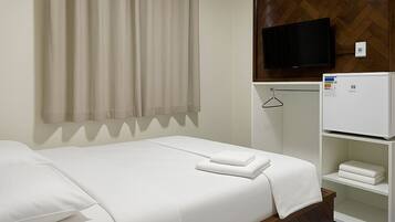 Habitación de hotel con cama, televisor, mini bar y panel de pared de madera.
