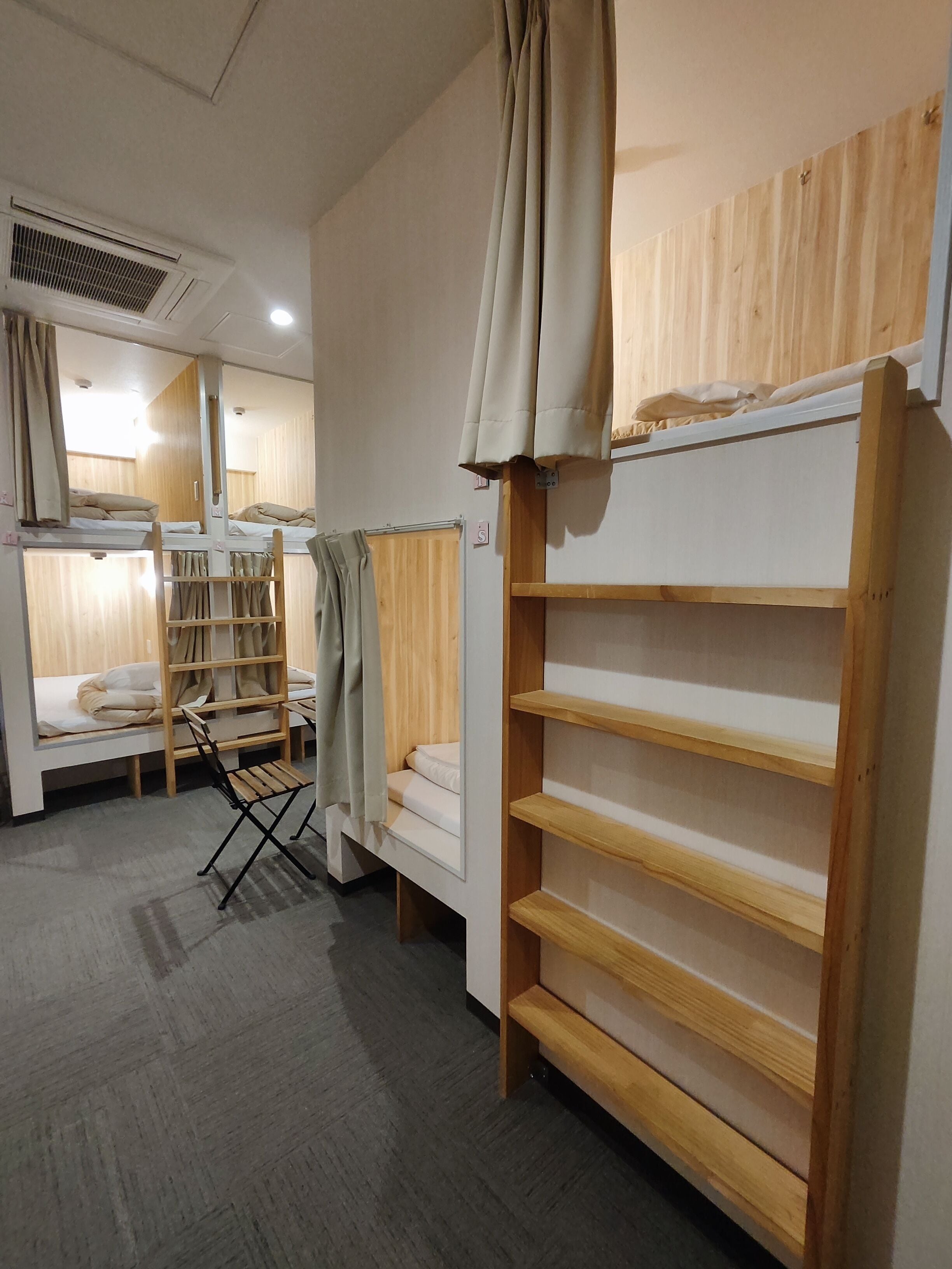 A compact hotel room with bunk beds, a foldable chair, and a wooden shelf unit.