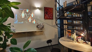 A modern interior with a wooden shelf, a black spiral staircase, and a projection screen displaying a light installation. - KOREGA Hostel Osaka Namba - Hostel (Osaka)