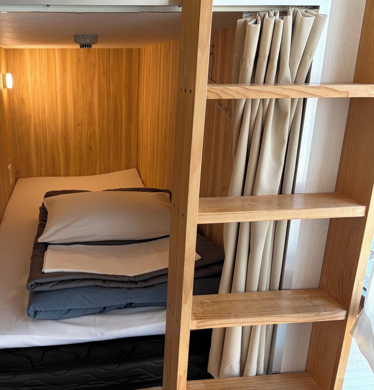 A wooden bunk bed with a shelf above containing rolled-up curtains.