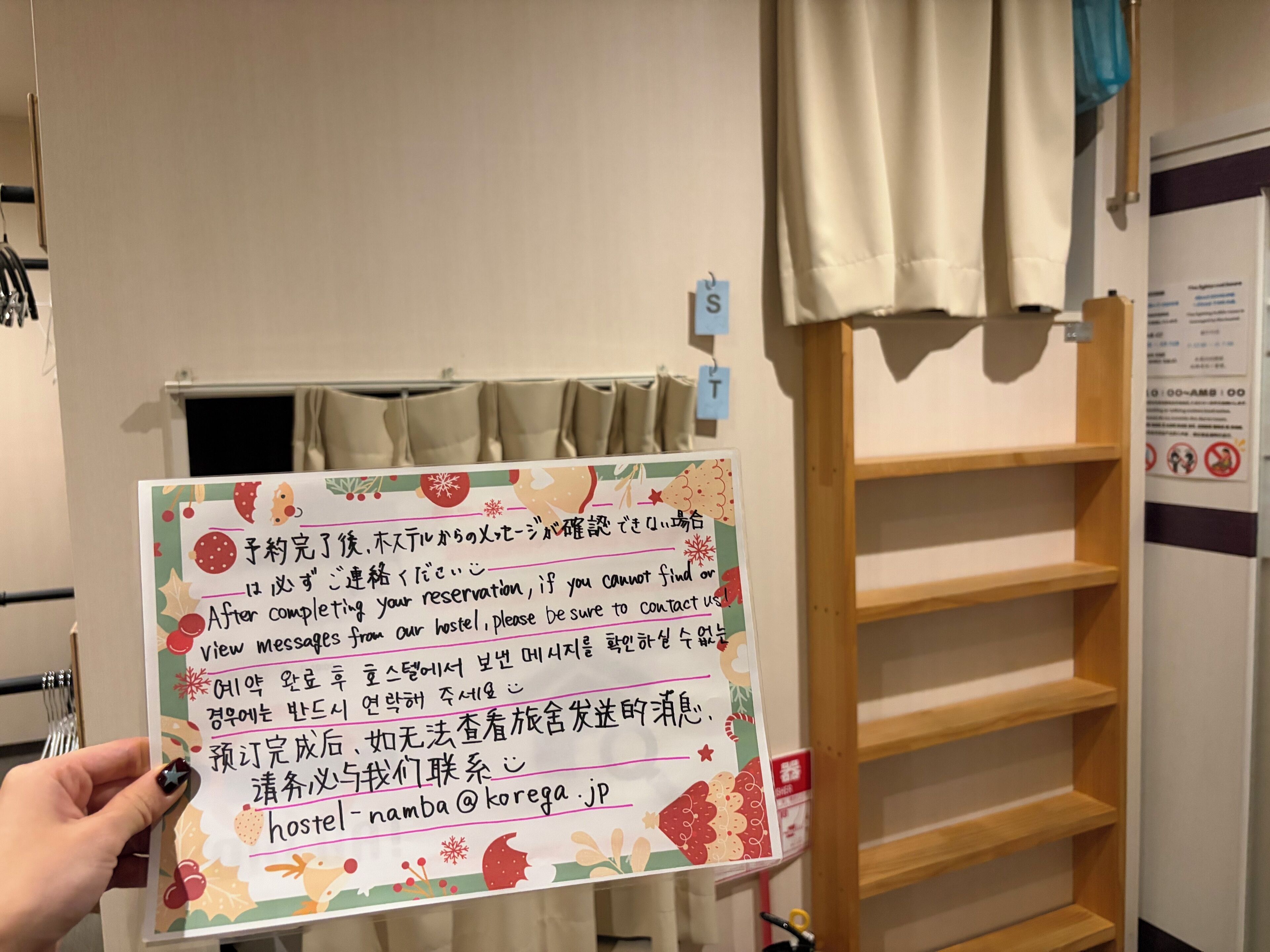 A hand holding a sign with text in a foreign language, a wooden shelf unit, and a curtain.