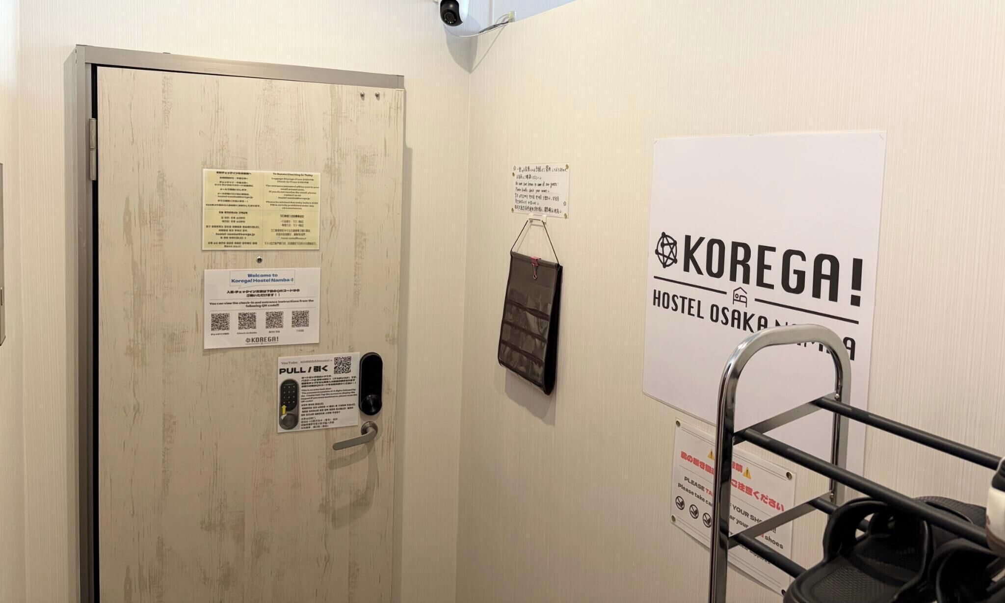Una puerta con varios avisos, un cartel de KOREGA! Hostel Osaka y un portaequipajes.