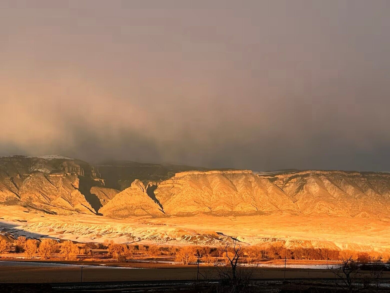 A mountainous landscape with a river in the foreground and a cloudy sky.