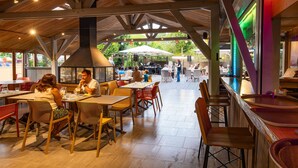 An outdoor dining area with wooden tables and chairs, a stage for live music, and a view of the garden.