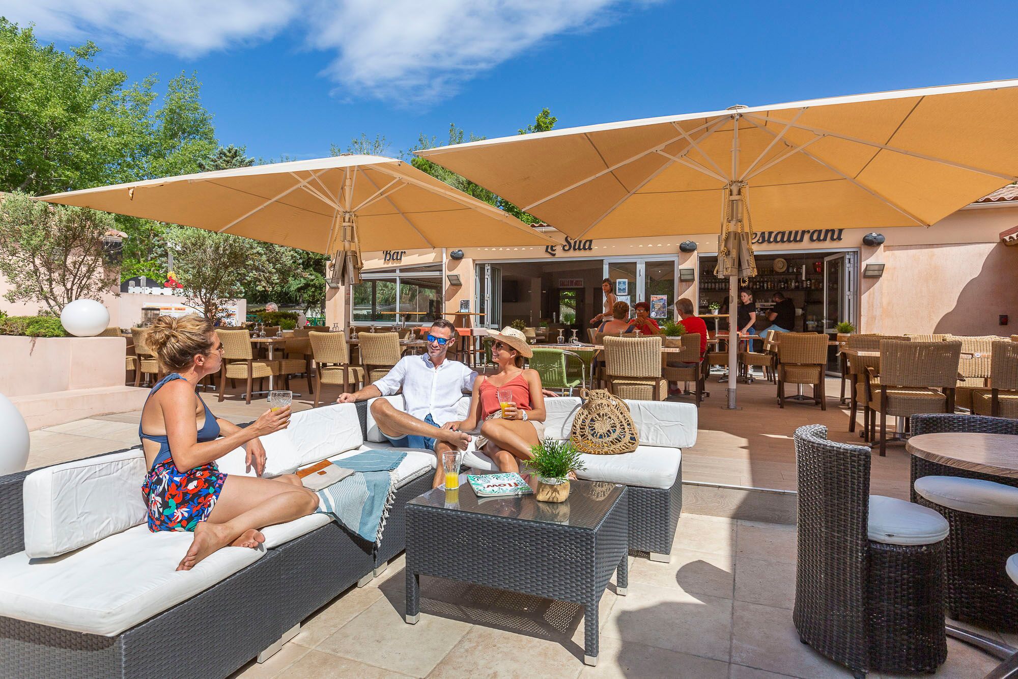 An outdoor seating area with wicker furniture and umbrellas, a bar, and a restaurant in the background.