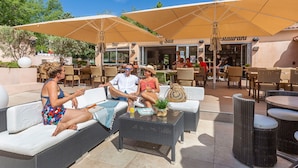 An outdoor seating area with wicker furniture and umbrellas, a bar, and a restaurant in the background.