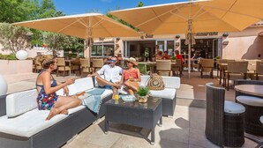 An outdoor seating area with wicker furniture and umbrellas, a bar, and a restaurant in the background.