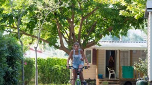 A person riding a bicycle on a paved path with trees and a house in the background.